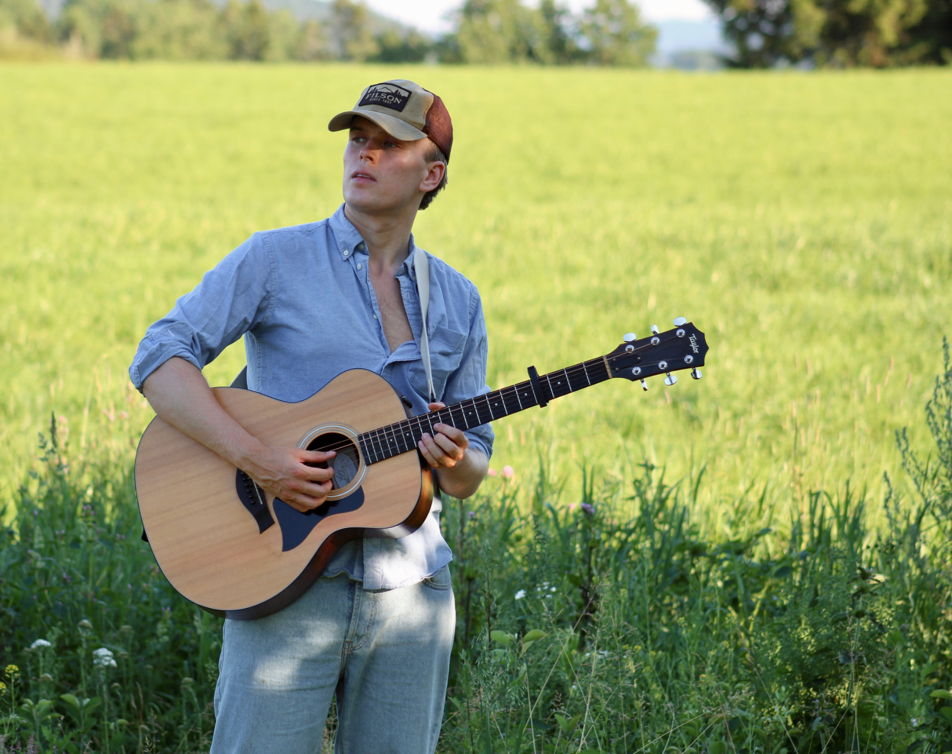 Sander Elstad med akustisk gitar i en grønn eng.